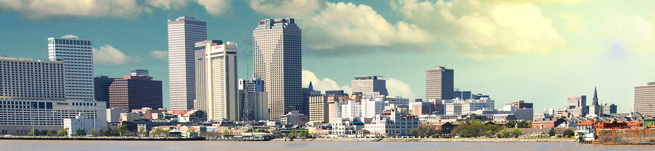 Skyline of New Orleans with various high-rise buildings, viewed from across a wide river under a partly cloudy sky.